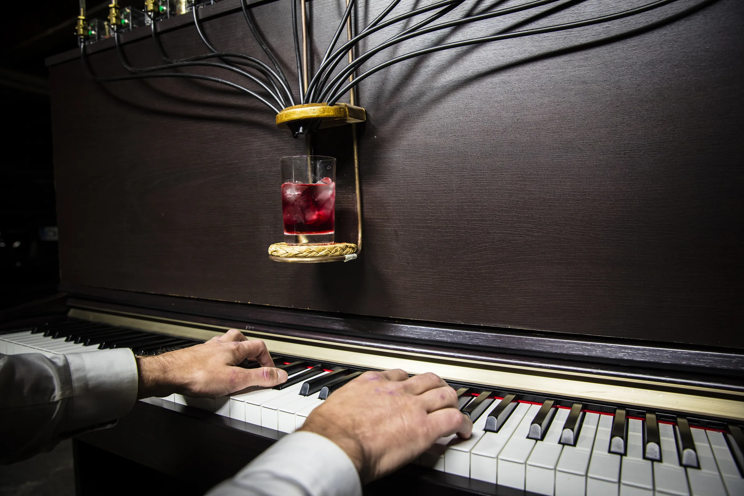 Mains du pianiste sur le clavier du Pianocktail, cocktail rouge au-dessus des touches