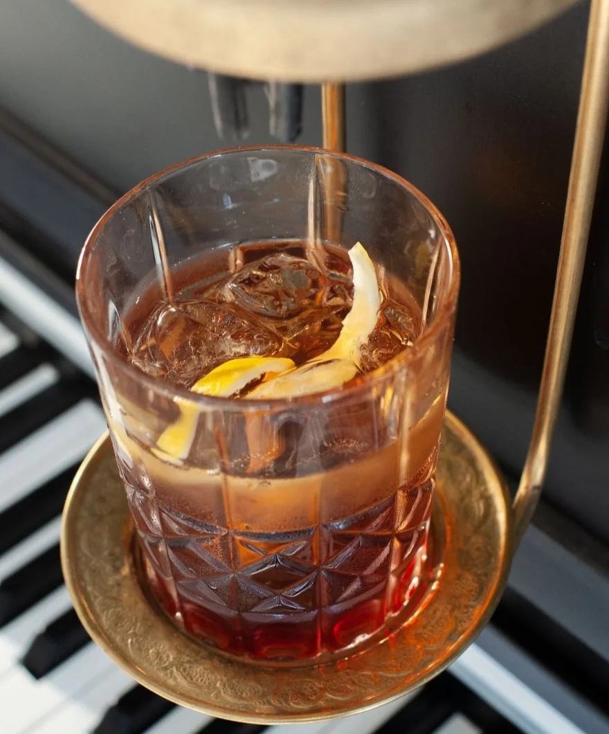 Verre de cocktail en cristal posé sur le présentoir doré du Pianocktail, au-dessus du clavier